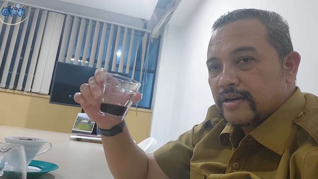 AKW mengangkat gelas berisi kopi robusta V60 hitam tanpa gula saat lembur di kantor